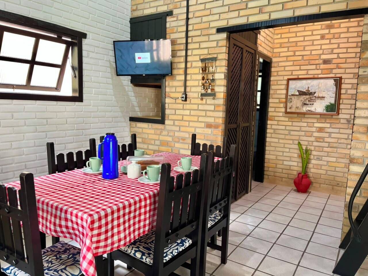 A dining area with a checkered tablecloth, black chairs, and a television mounted on the wall.