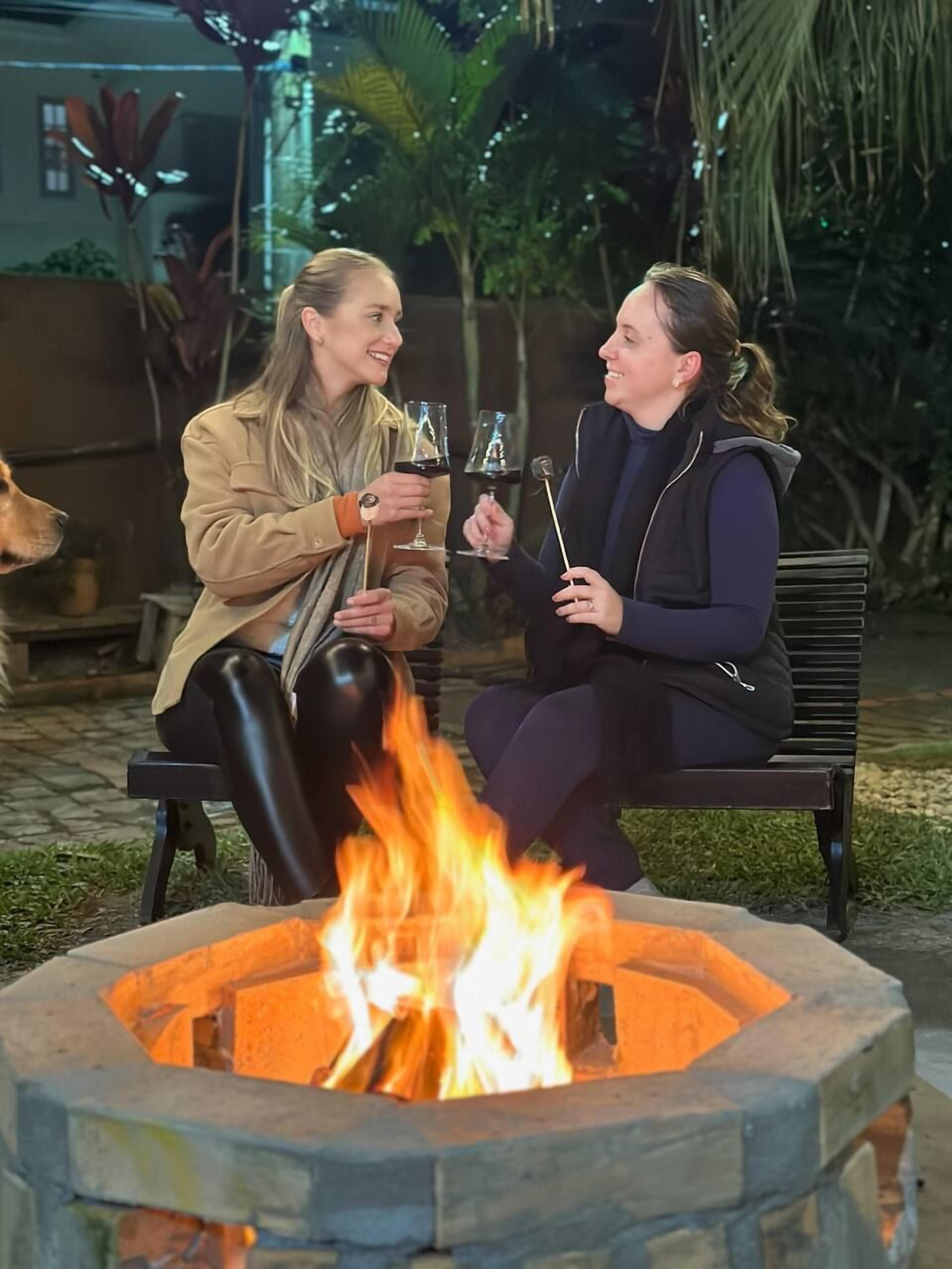 Two people sitting on a bench near a fire pit.