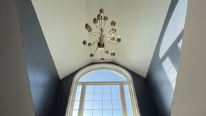 Ein Zimmer mit hohen Decken, einer Kandelaber, einem großen Fenster und Buntglasfenstern.