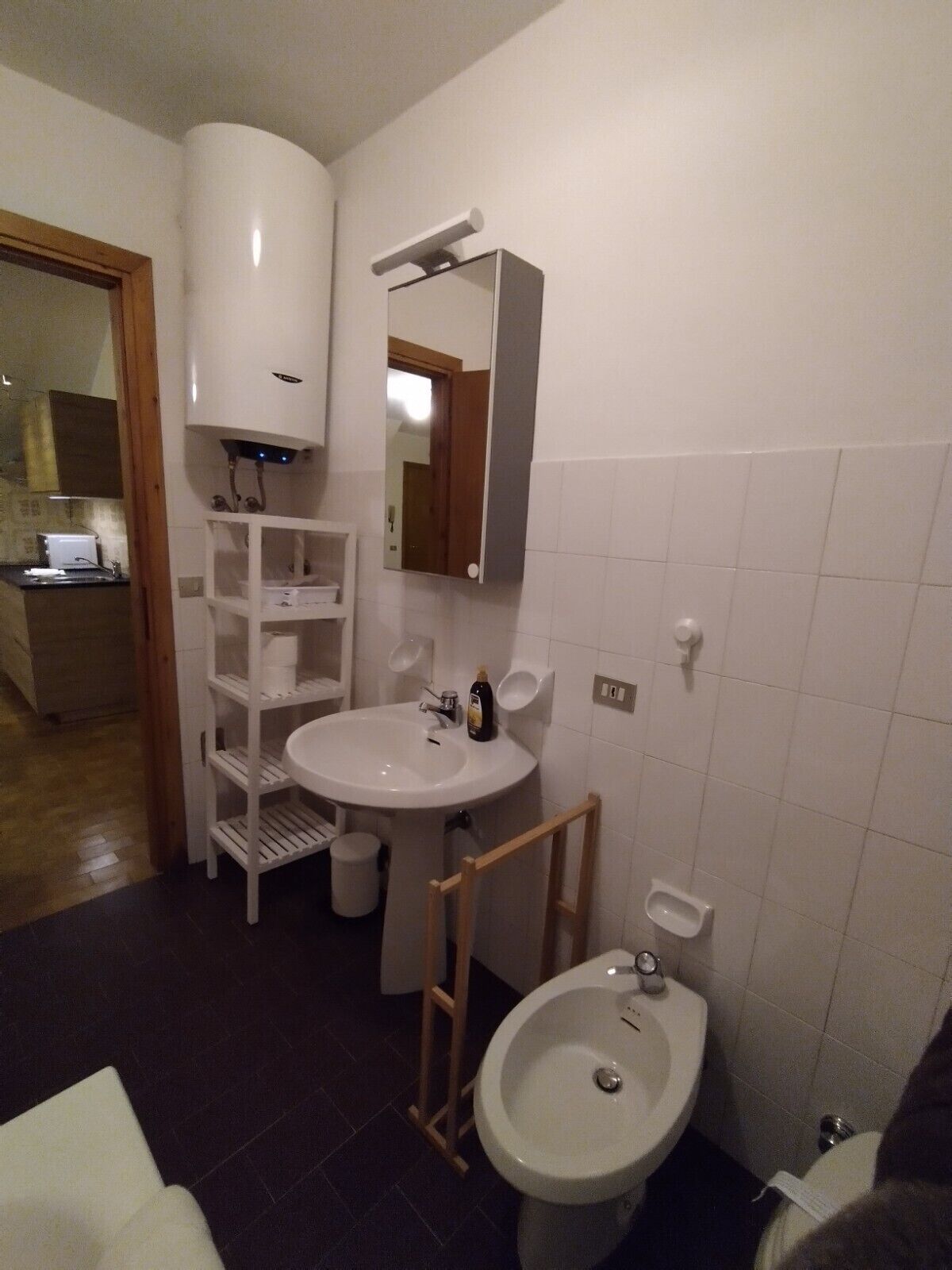 Un baño con un lavabo blanco, un espejo, un inodoro y un bidé. Una escalera de madera está apoyada contra la pared cerca del inodoro.