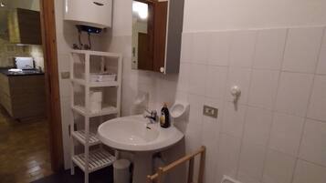 Un baño con un lavabo blanco, un espejo, un inodoro y un bidé. Una escalera de madera está apoyada contra la pared cerca del inodoro.