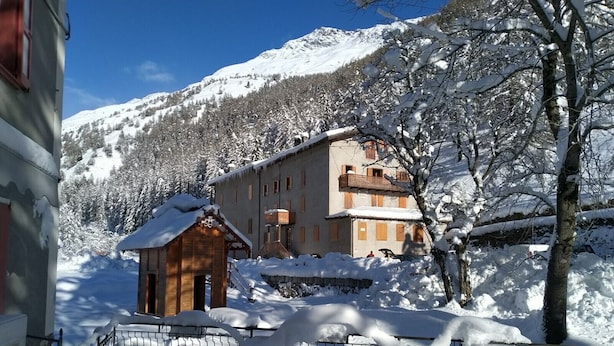 Un edificio cubierto de nieve con una estructura de madera al frente, rodeado de árboles nevados y una montaña al fondo.