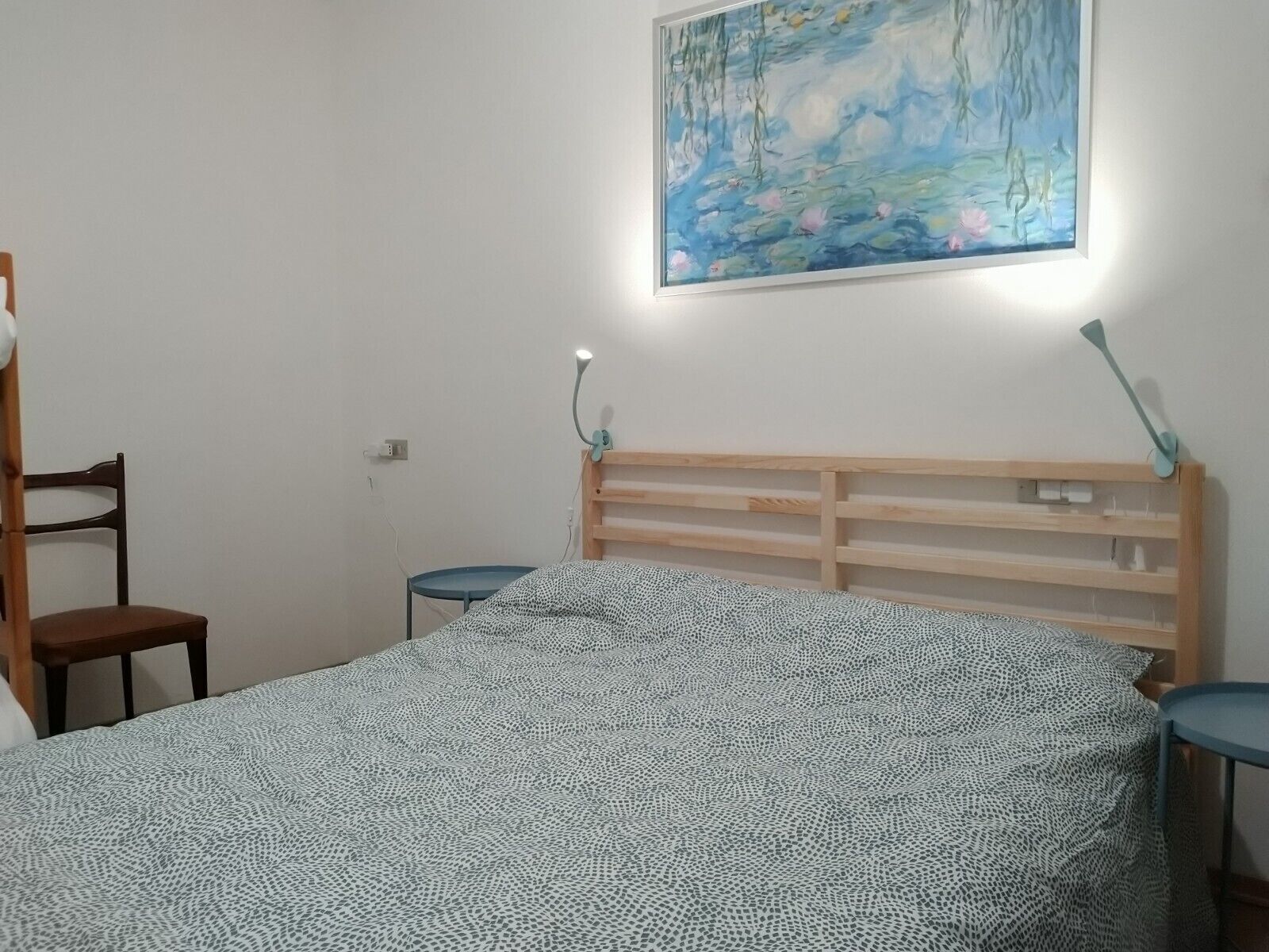 Ein Schlafzimmer mit einem Bett, einem Sessel, einem Nachttisch, einer Lampe und einem Bild an der Wand.