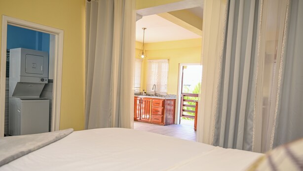 A bedroom with a bed, a kitchenette with wooden cabinets, and a view of the outside through a doorway. - Eden Villas (Corinth)