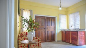 A room with a wooden door, a sink, a countertop, a patterned sofa, a table with a plant, and a hanging light fixture. - Eden Villas (Corinth)