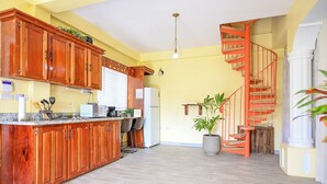 A kitchen with wooden cabinets, a central island, a refrigerator, and a red spiral staircase. - Eden Villas (Corinth)
