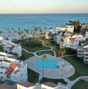 A resort with a central pool, surrounded by palm trees and a view of the ocean.