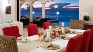A dining area with a view of the ocean, red chairs, a white tablecloth, and decorative centerpieces. - Luxury 4 Bedroom, 7 Bathroom Villa on Shoal Bay, Anguilla (Shoal Bay)