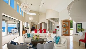 A spacious living area with a large sectional sofa, a coffee table with a floral centerpiece, and a view of the ocean through large windows. - Luxury 4 Bedroom, 7 Bathroom Villa on Shoal Bay, Anguilla (Shoal Bay)