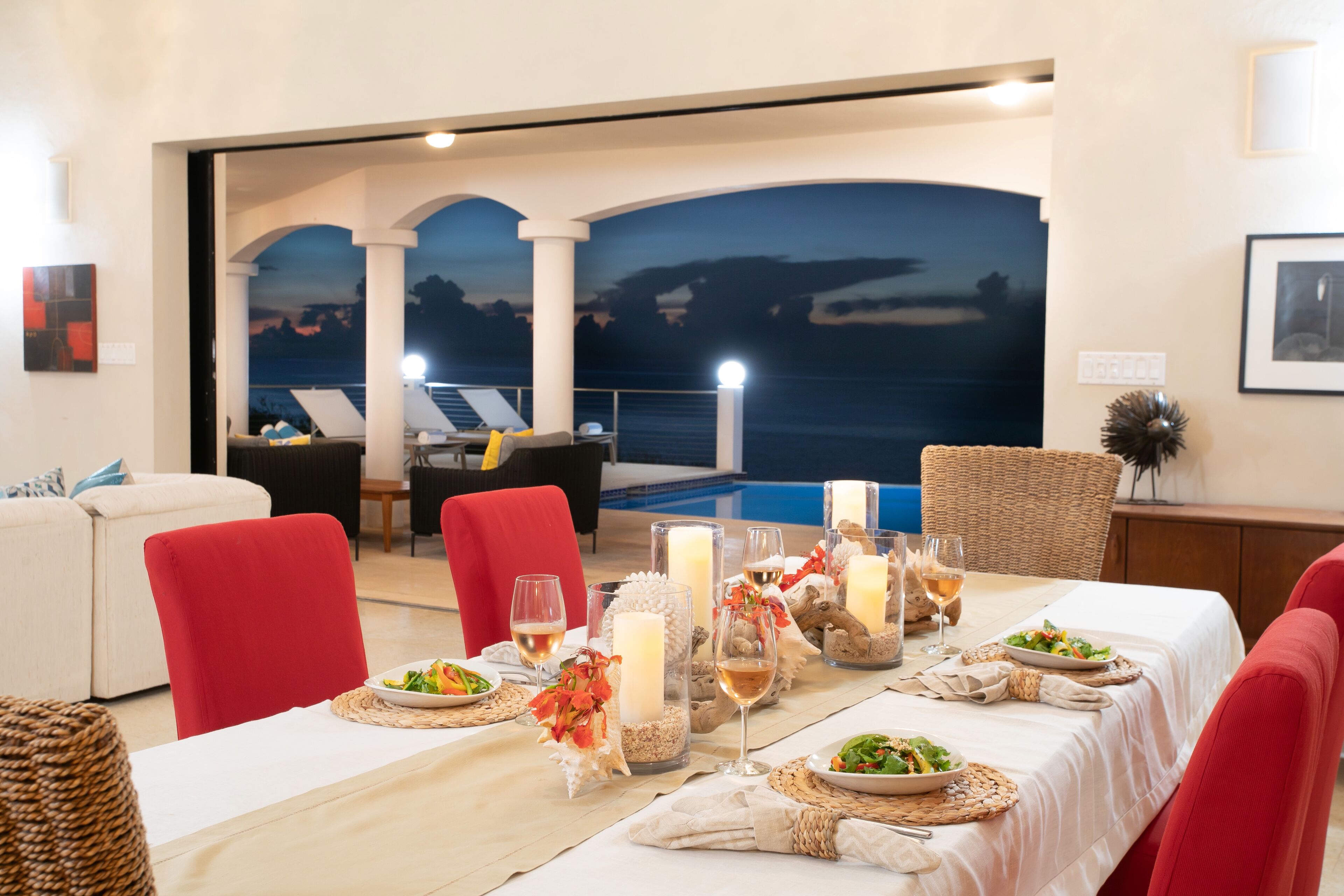 A dining area with a view of the sea, a pool, and a sunset mural.