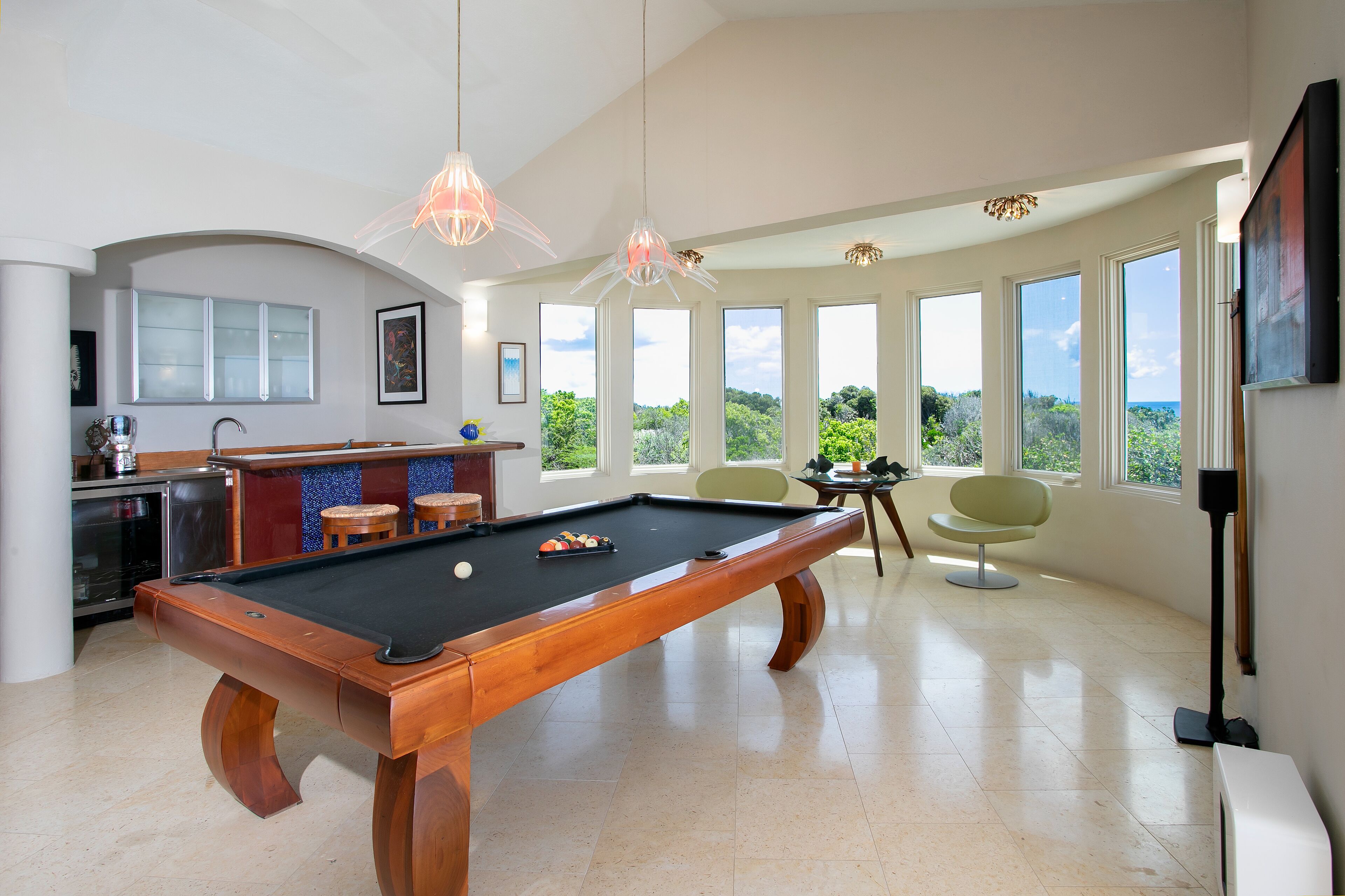 A pool table in a spacious room with large windows offering a view of greenery.
