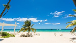 Ein Strand mit weißem Sand, Palmen und wolkenlosem, blauem Himmel.