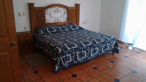 A bedroom with a wooden headboard, a patterned bedspread, a small bedside table, and a tiled floor. - ZONA DORADA BALBOA APARTAMENT 1 (Mazatlán)