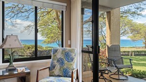 A room with a view of the ocean, a chair with a tropical print, and a lamp on a side table.