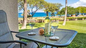 A table with a bottle of wine and two glasses, set outdoors with a view of the ocean and palm trees.