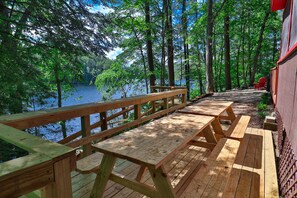 Terraza de madera con mesas de picnic que da a un lago, rodeada de árboles.