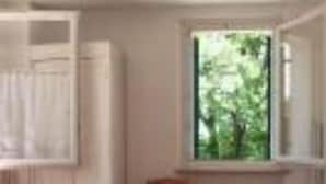 Ein Zimmer mit einem Bett, einem Fenster mit Blick auf Grünflächen, einem Stuhl und einem weißen Kleiderschrank.