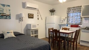 A compact bedroom with a bed, bedside table, and a small kitchenette with a refrigerator, microwave, and stove.