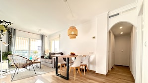 A modern living room with a dining area, wooden flooring, and a view through large windows. - Anacasa Les Marines Puerta del Palmar AP2207 (Denia)