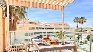 A balcony with a table set for breakfast, overlooking a residential area with palm trees and a pool. - Anacasa Les Marines Puerta del Palmar AP2207 (Denia)