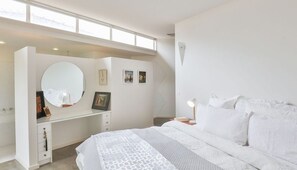A modern bedroom with a large bed, a vanity with a mirror, and a desk.
