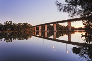 A bridge over a calm body of water with trees and streetlights.