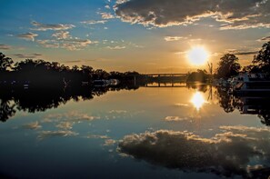 Een rustige rivier die de zonsondergang weerspiegelt, met een brug en bootjes in de verte.
