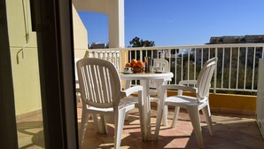 Un balcón con una mesa dispuesta para dos, sillas de plástico blanco y una cesta de naranjas.