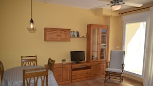 Una sala de estar con un aparador de madera, un televisor, una mesa de comedor con sillas y una mesa de centro de vidrio.