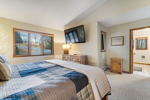 A bedroom with a large bed, a TV mounted on the wall, a dresser, and a small cabinet.