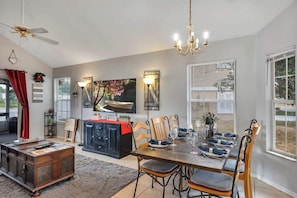 A dining area with a wooden table set for six, surrounded by wooden chairs. There is a black cabinet with a red cloth, a ceiling fan, and a chandelier. - Chill 4/2, Lakefront, Game Room, Fishing & Hot Tub (Oviedo)