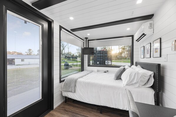 Un dormitorio con cama, televisor y una ventana grande.