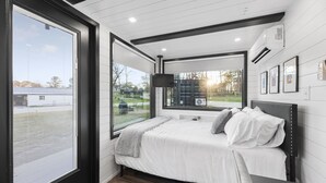 A bedroom with a bed, a TV, and a large window. - Combo Plate: 2 mins to Lake Conroe! Heated Pool, Stocked Ponds, Cute Pygmy Goats (Willis)