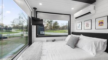 Relax in this serene bedroom with a large bed against a window overlooking a park with trees and a pathway.