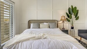 Een moderne slaapkamer met een groot bed, een nachtkastje met lamp en een potplant.
