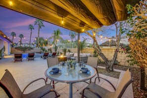 Eine Terrasse mit runden Tischen und Stühlen, einer Feuerstelle und Lichterketten.