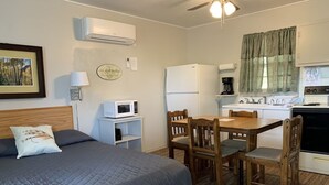 A bedroom with a bed, bedside table, lamp, and a kitchenette with a refrigerator, stove, and microwave. - All is Just Fine in Cabin 9 (Cassville)