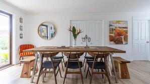 Ein Esszimmer mit Holztisch und -stühlen, einem Spiegel, einer Blumenvase und einem Gemälde an der Wand.