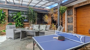 Un patio al aire libre con mesa de ping pong, mobiliario de mimbre y diversas plantas.