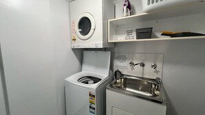 A laundry area with a washing machine, a dryer, and a sink with a sign requesting iron to be emptied after use. - Avenues Unit 1 (South West Rocks)