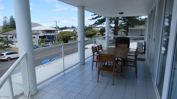 A balcony with a table and chairs, a view of the street, and houses in the background. - Avenues Unit 1 (South West Rocks)