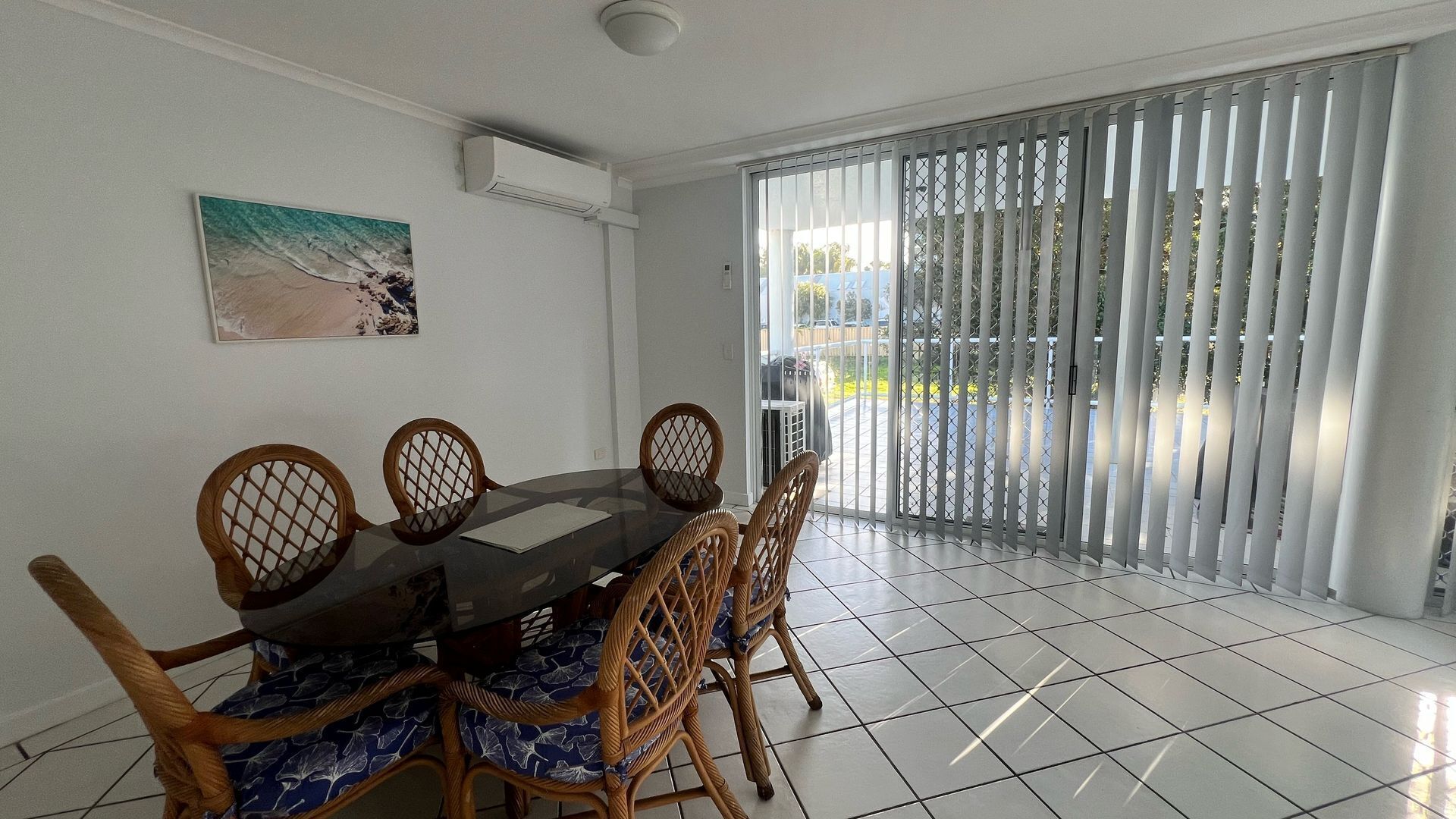 A dining area with a round table and six chairs, a painting on the wall, and a sliding glass door leading to an outdoor area.