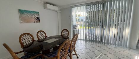 A dining area with a round table and six chairs, a painting on the wall, and a sliding glass door leading to an outdoor area.
