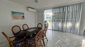 Un comedor con una mesa redonda y seis sillas, un cuadro en la pared y una puerta corredera de vidrio que da a un espacio exterior.
