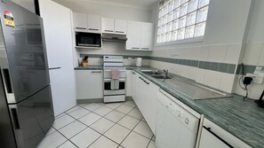 Et køkken med hvide skabe, et rustfrit stål køleskab, en mikrobølgeovn, en ovn, en vask og et vindue med udsigt.