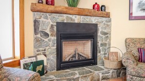 Una chimenea de piedra con un marco negro, un repisa de madera encima y un cuadro en la pared.