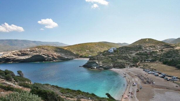 A coastal area with a beach, rocky terrain, and a small building. - Summer Sunrice Andros (Andros)