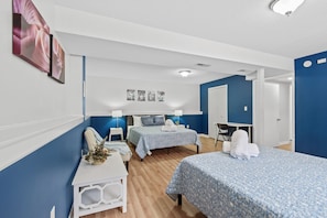 A hotel room with two beds, a desk, and a chair. There are wall-mounted lamps and a ceiling light.