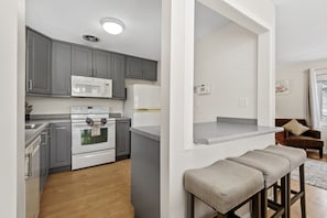 A modern kitchen with grey cabinets, white appliances, and a wooden floor.