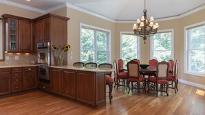 A spacious kitchen with wooden cabinets, a central island, and a dining area with red chairs and a chandelier. - Bridgehampton gem in private community- 1 mile from the village (Bridgehampton)